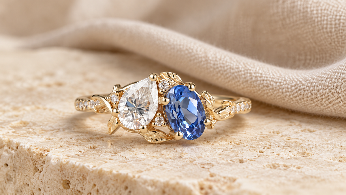 Toi et moi ring featuring a pear-shaped clear gemstone and an oval blue gemstone in a yellow gold leaf setting
