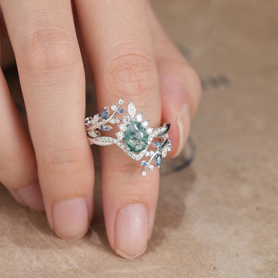 Moss agate pear ring with sapphire and leaf accents on a model's hand.