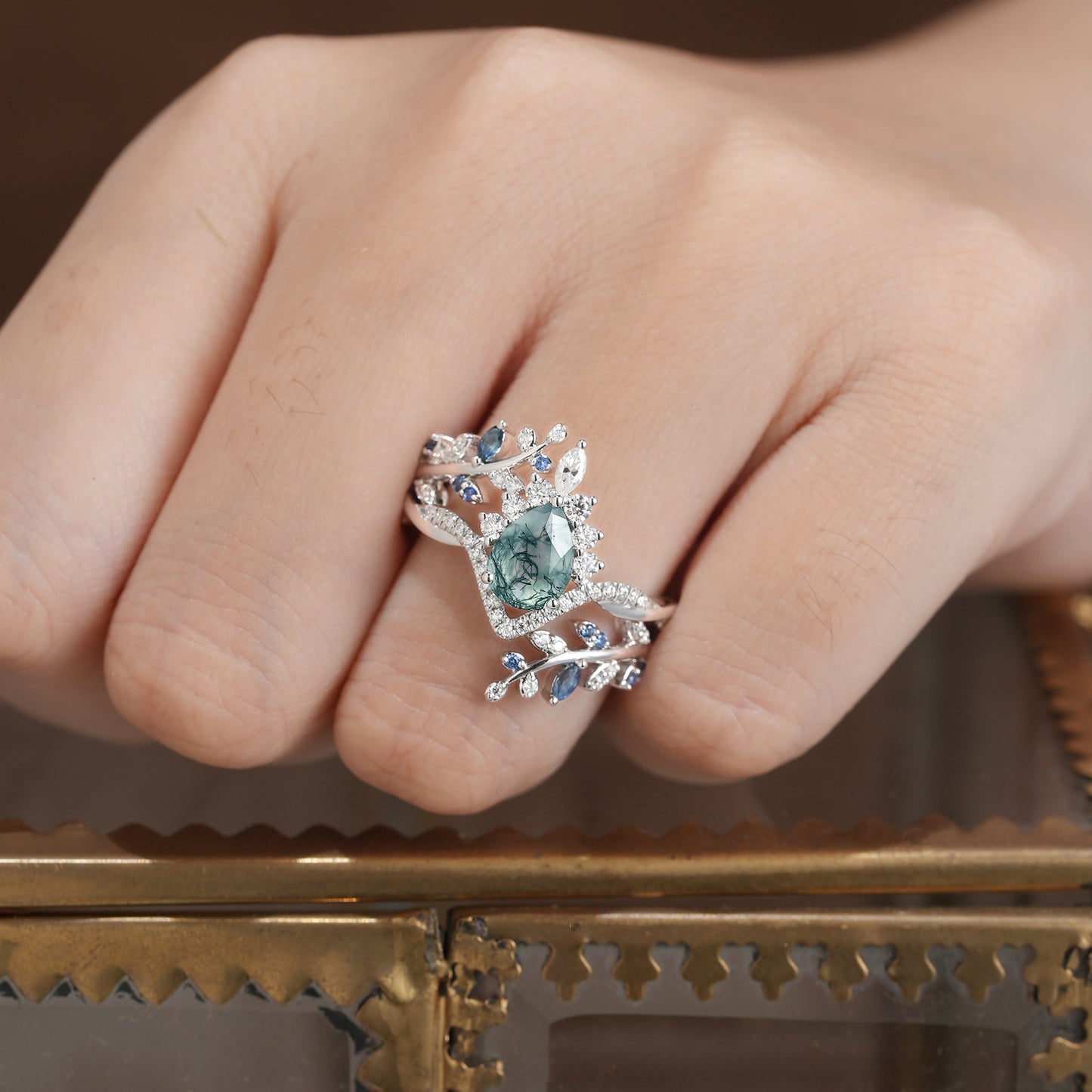 Moss agate crown ring set with sapphire in leaf design on a model's hand.