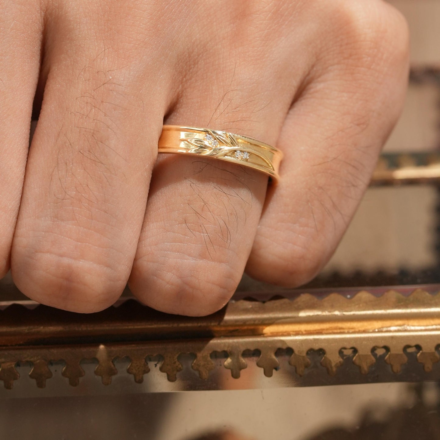 Gold men's band featuring leaf motifs and diamond accents on a hand.