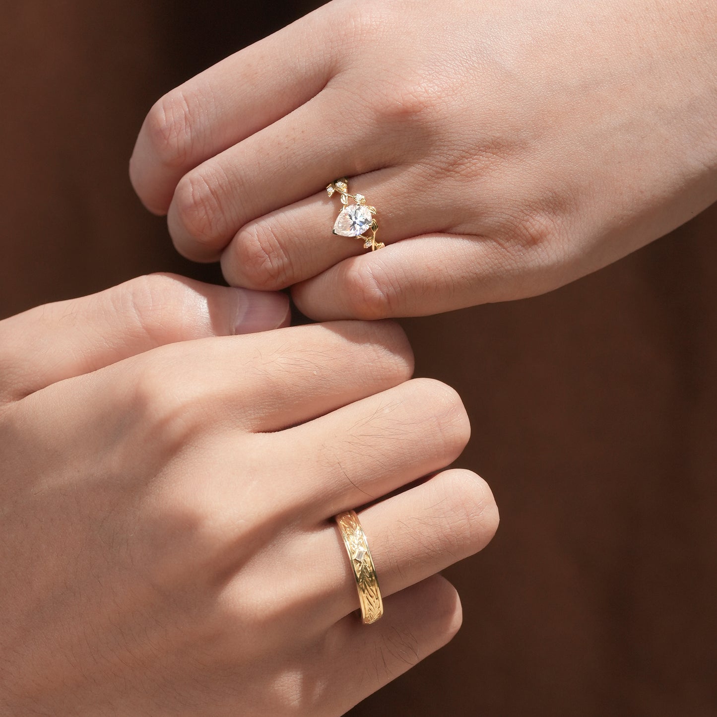 Couple's hands featuring vine-inspired moissanite engagement ring and textured wedding band.