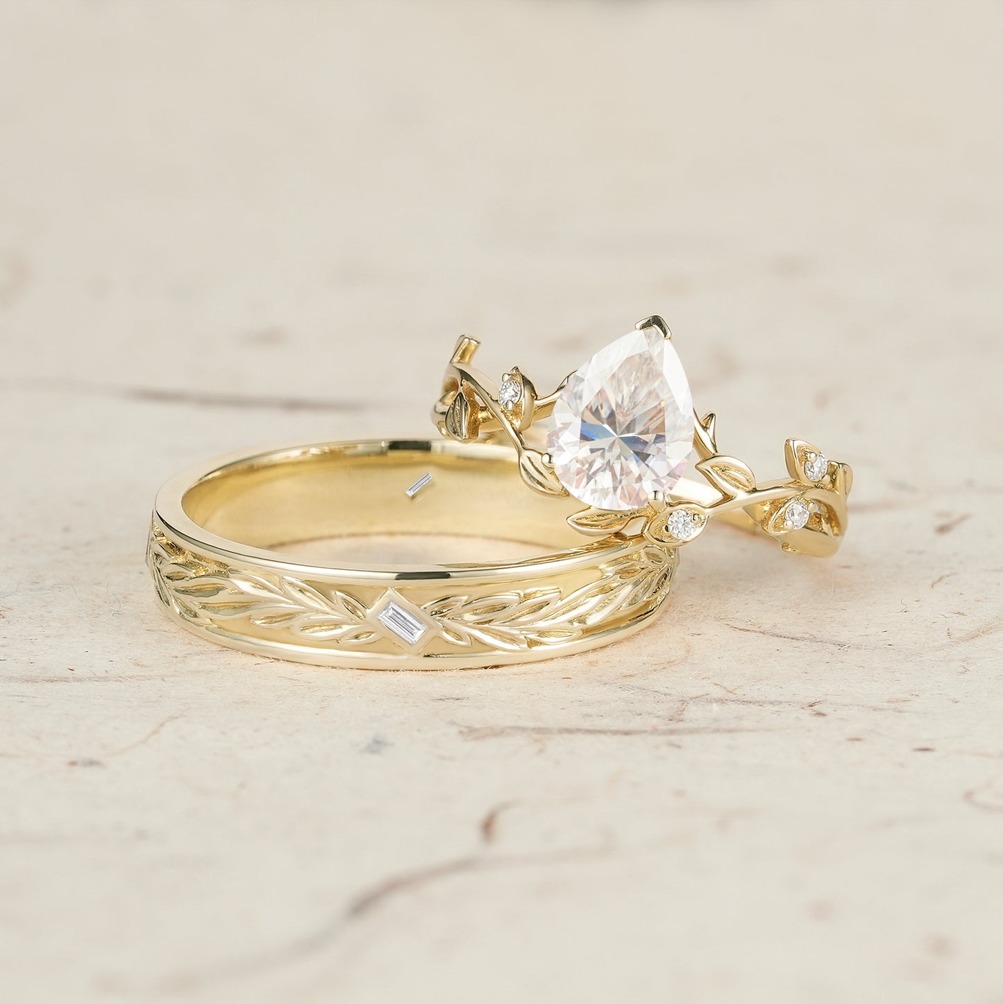 Moissanite couple ring set showcasing pear-cut stone and vine design in yellow gold.