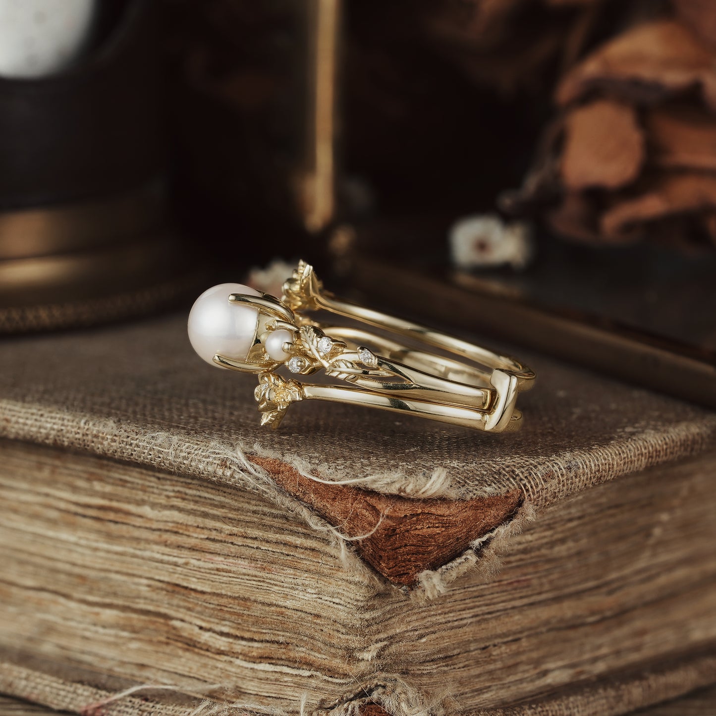 Gold floral ring set featuring Akayo pearl and moissanite accents on a rustic book