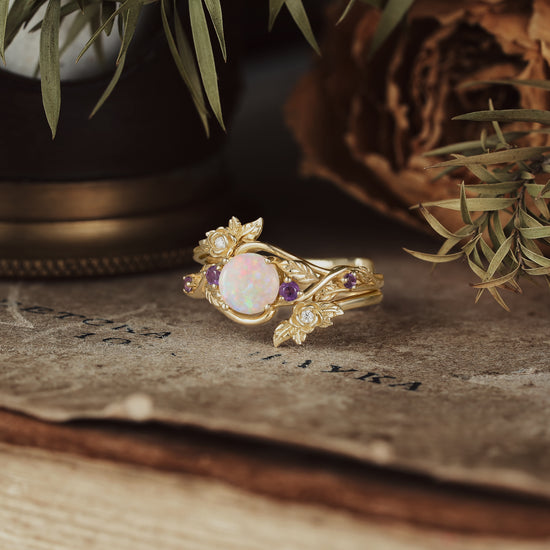 Nature-inspired opal ring set with amethyst and gold floral accents on rustic background.