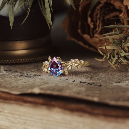 Nature-inspired alexandrite ring with intricate leaf design on textured background.