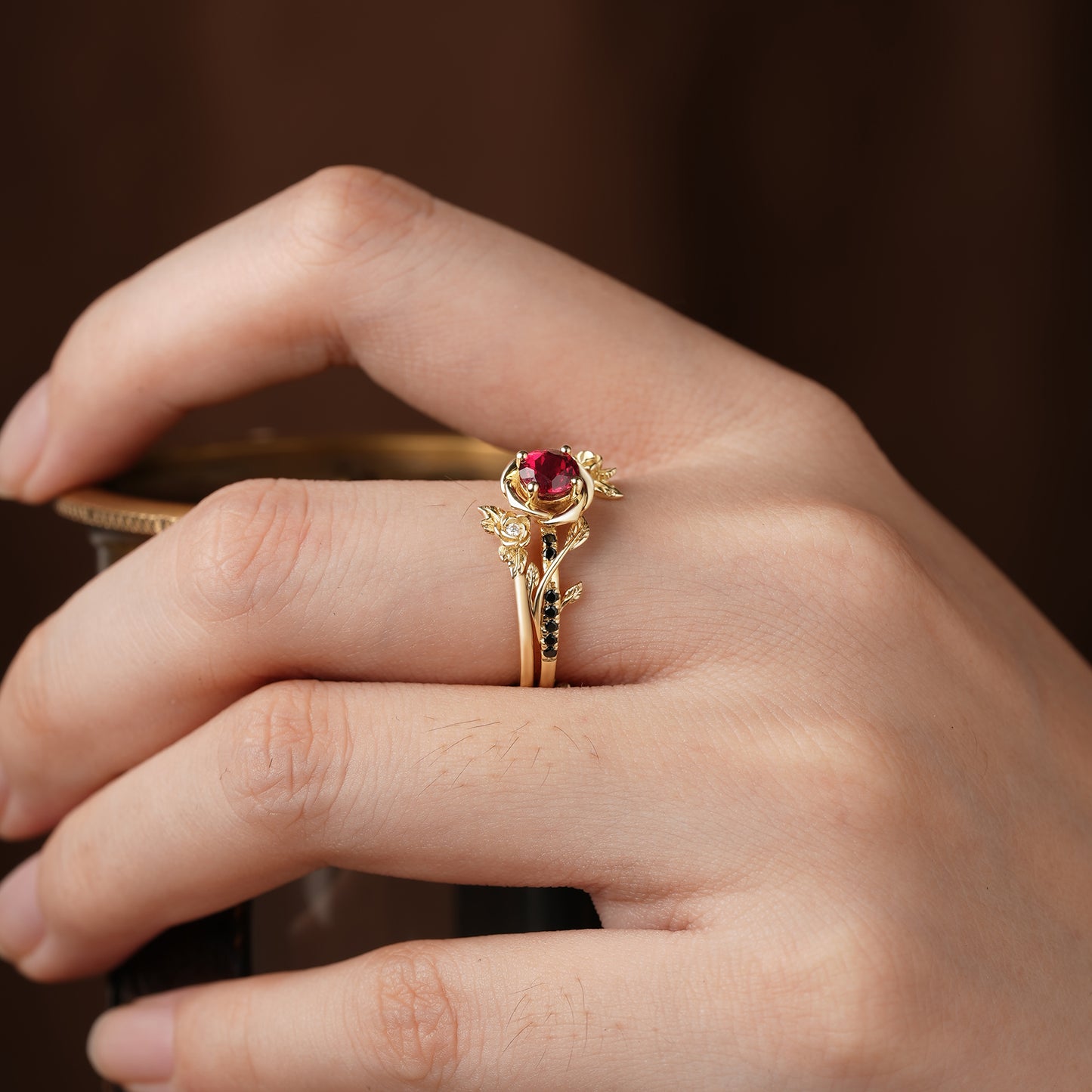 Hand showcasing Rose Blossom ruby ring with gold embellishments and central ruby.