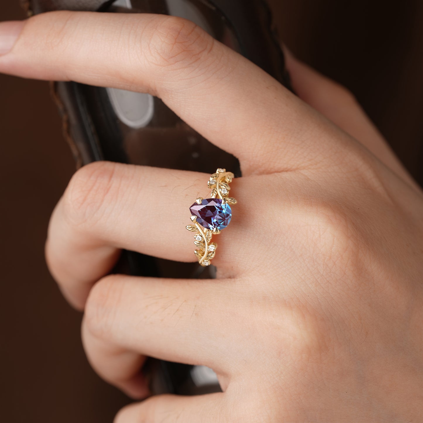 Elegant alexandrite ring with leaf details worn on a hand holding a phone