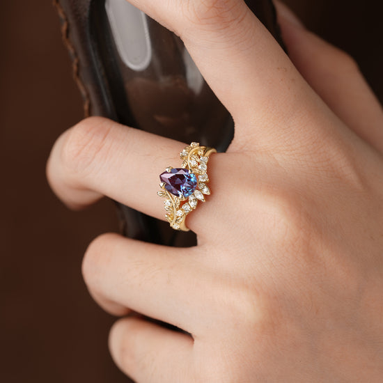 Gold ring set with pear-cut alexandrite and leaf accents worn on a hand