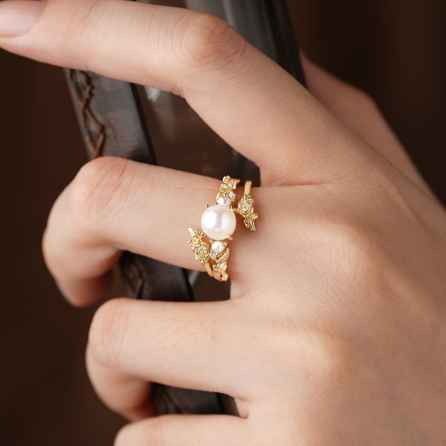 Hand showcasing Rose Blossom pearl ring set with floral accents and Akayo pearl centerpiece.