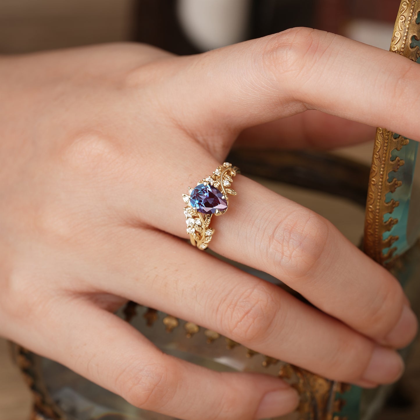 Elegant gold alexandrite ring with intricate leaf design worn on a hand