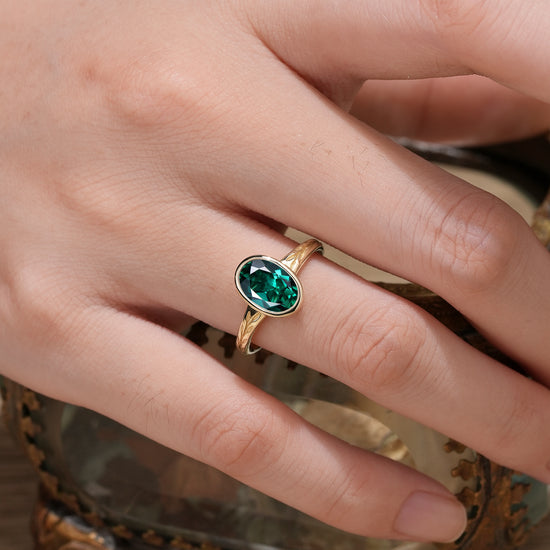 Gold ring with oval emerald and leaf design on hand showcasing nature-inspired elegance.