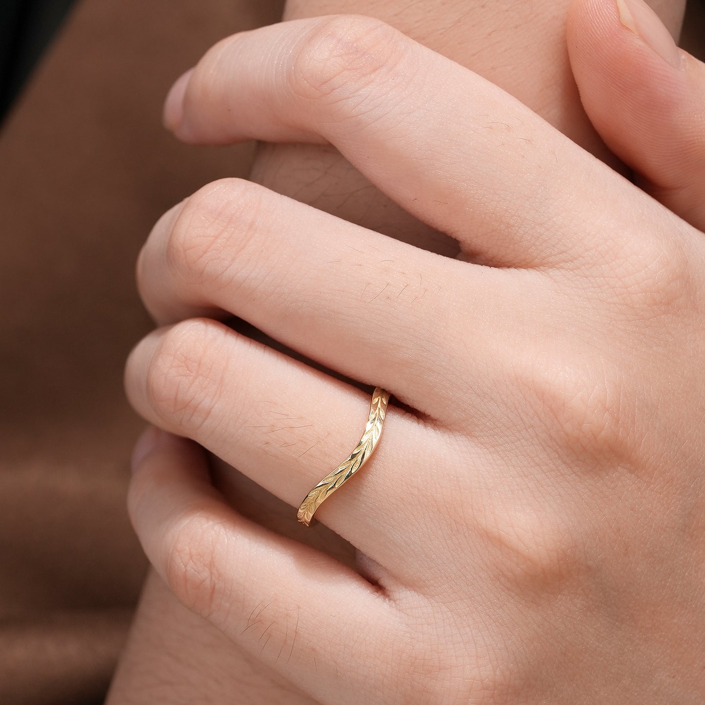 Twisted gold ring with leaf design accentuating hand resting elegantly.