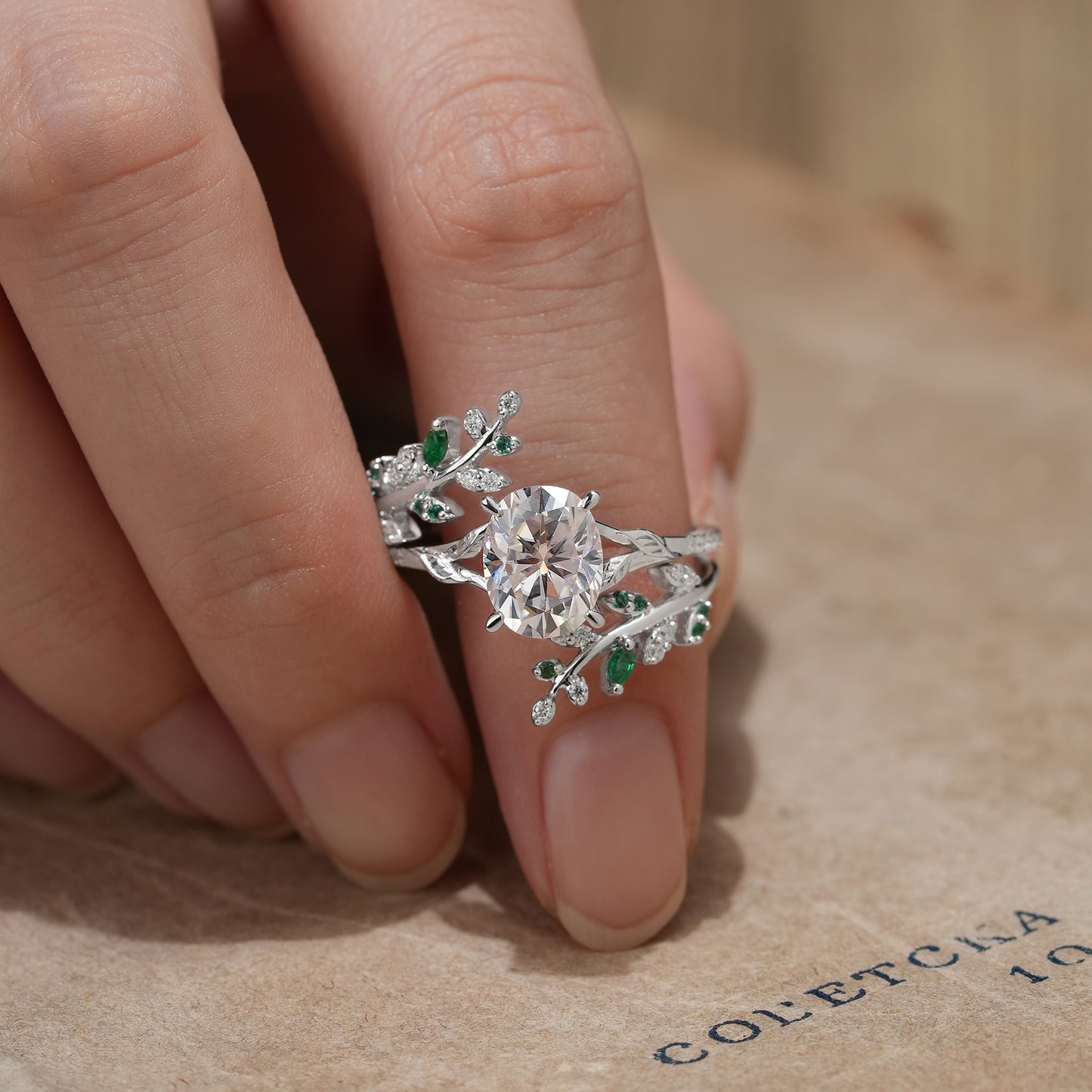 Oval moissanite engagement ring with emerald accents on a leaf-inspired band