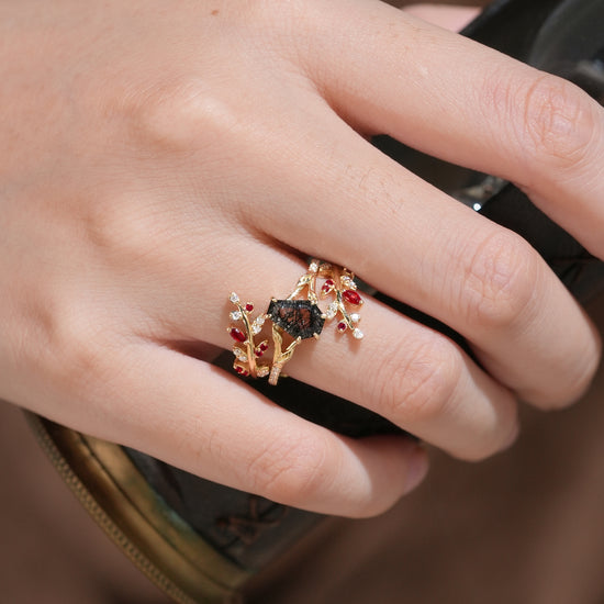 Nature-inspired black rutilated quartz ring set with rubies, displayed on a hand.