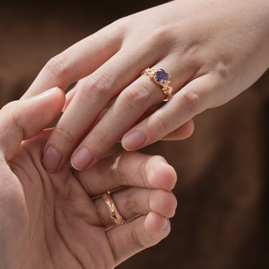 Couple's hands with heart-shaped alexandrite ring and rose gold wedding band.