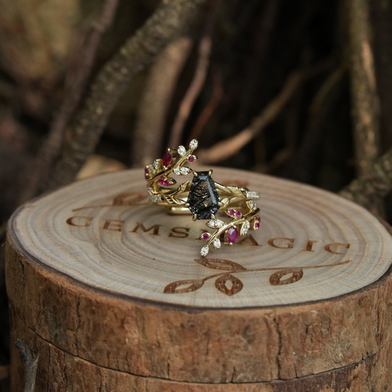 Black rutilated quartz ring set with rubies on a twined gold band, placed on wood.