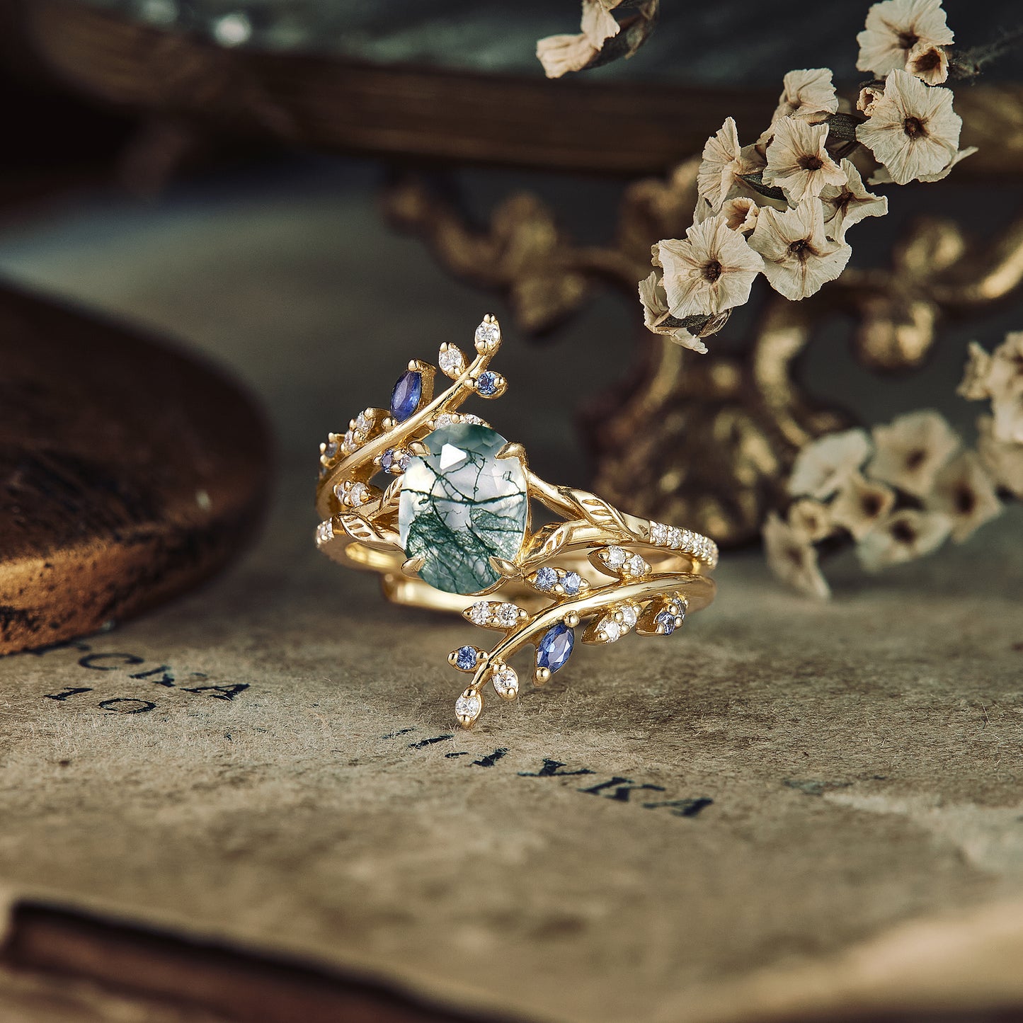 Gold vine engagement ring with moss agate and sapphire surrounded by decorative elements