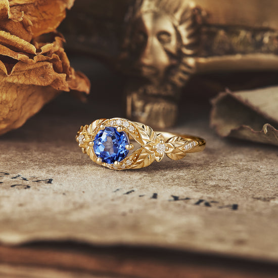 Gold band engagement ring with a round lab-grown sapphire and intricate leaf design.