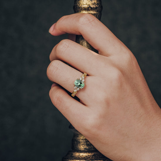 Hand wearing oval cut green sapphire leaf ring on textured gold band with moissanite.