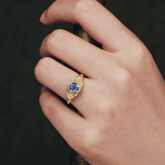 Yellow gold engagement ring with central lab-grown sapphire and intricate leaf design.