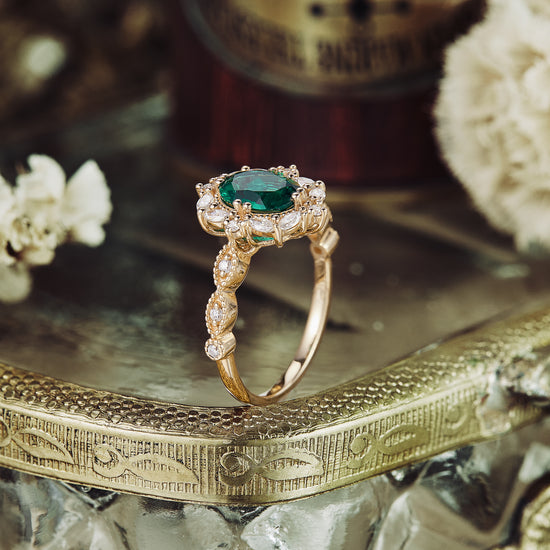 Vintage gold engagement ring with emerald and diamond accents on textured display.