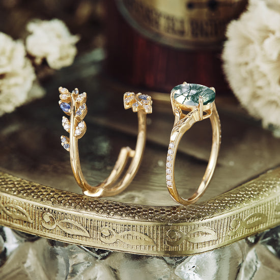 Moss agate engagement ring and sapphire band with intricate vine design on decorative tray.