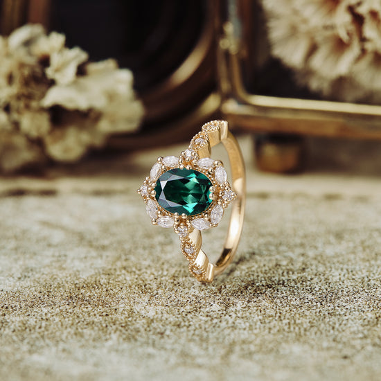 Emerald and diamond vintage-style engagement ring on textured surface.