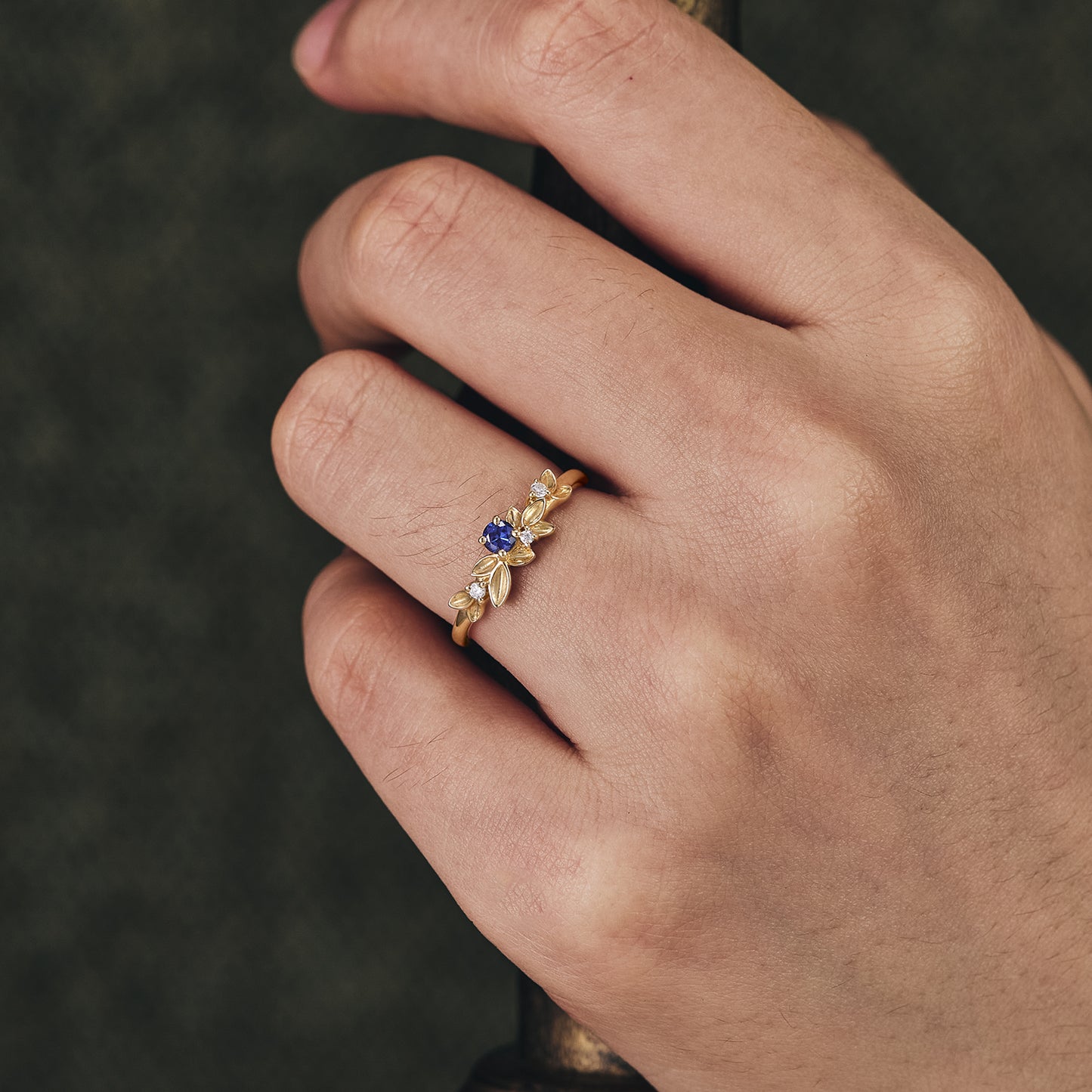 Gold wedding band with sapphire and moissanite, featuring intricate leaf details.