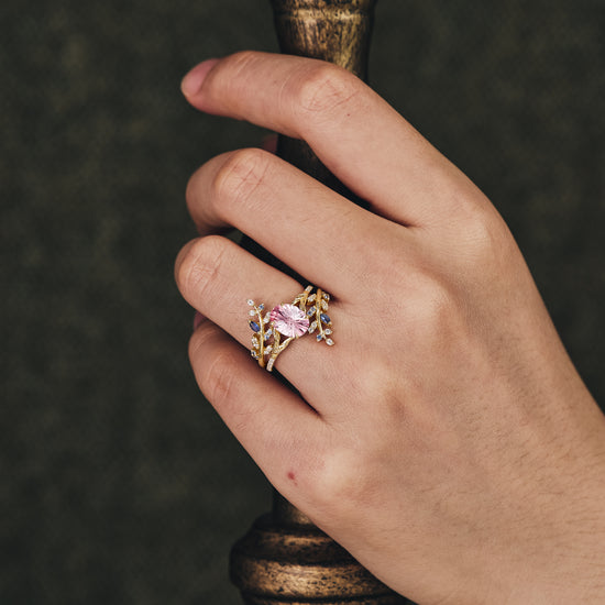 Nature-inspired Padparadscha engagement ring set on a hand with gold vine accents.