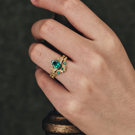 Nature-inspired gold ring with pear-cut lab emerald and green stone accents.