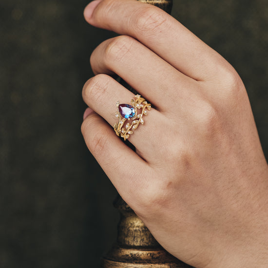 Nature-inspired pear cut alexandrite ring set with leaf details worn on a hand.