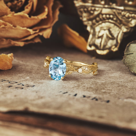 Aquamarine engagement ring in ornate gold setting on textured background.