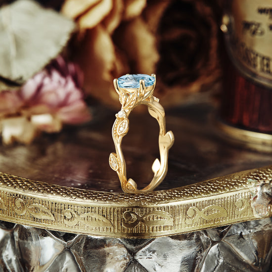 Vintage aquamarine engagement ring with nature-inspired gold band on ornate tray.