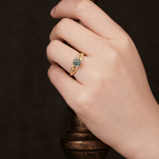 Hand wearing textured twig ring with round lab-grown green sapphire centerpiece.