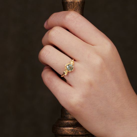 Hand wearing Beekeeper Garden Ring with round green sapphire and leaf details.