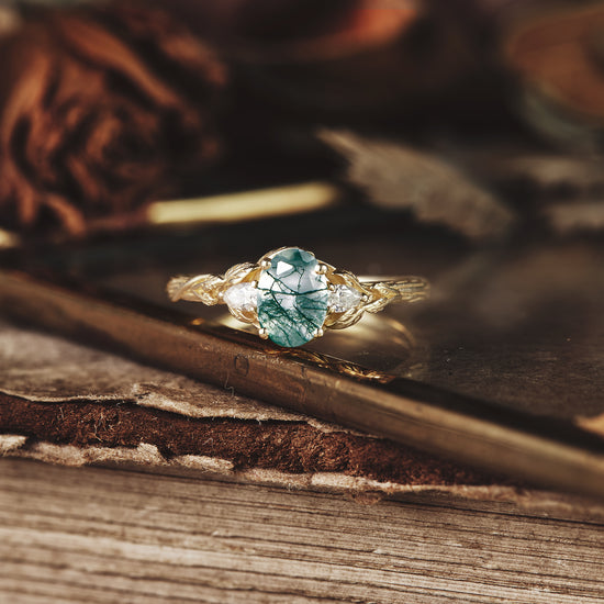 Three-stone moss agate engagement ring with moissanite accents on a wooden surface