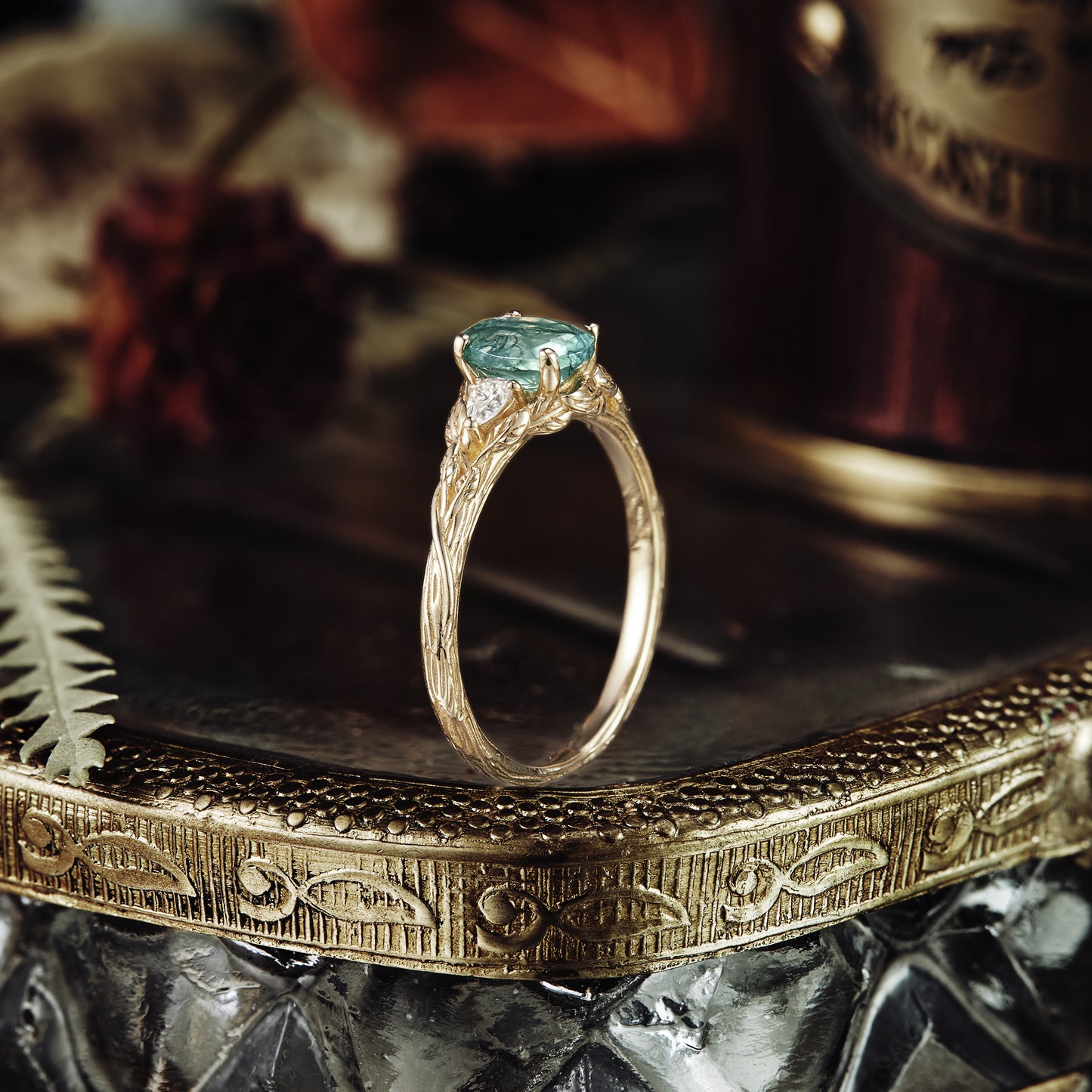 Three-stone moss agate engagement ring on a decorative gold tray, showcasing intricate details.