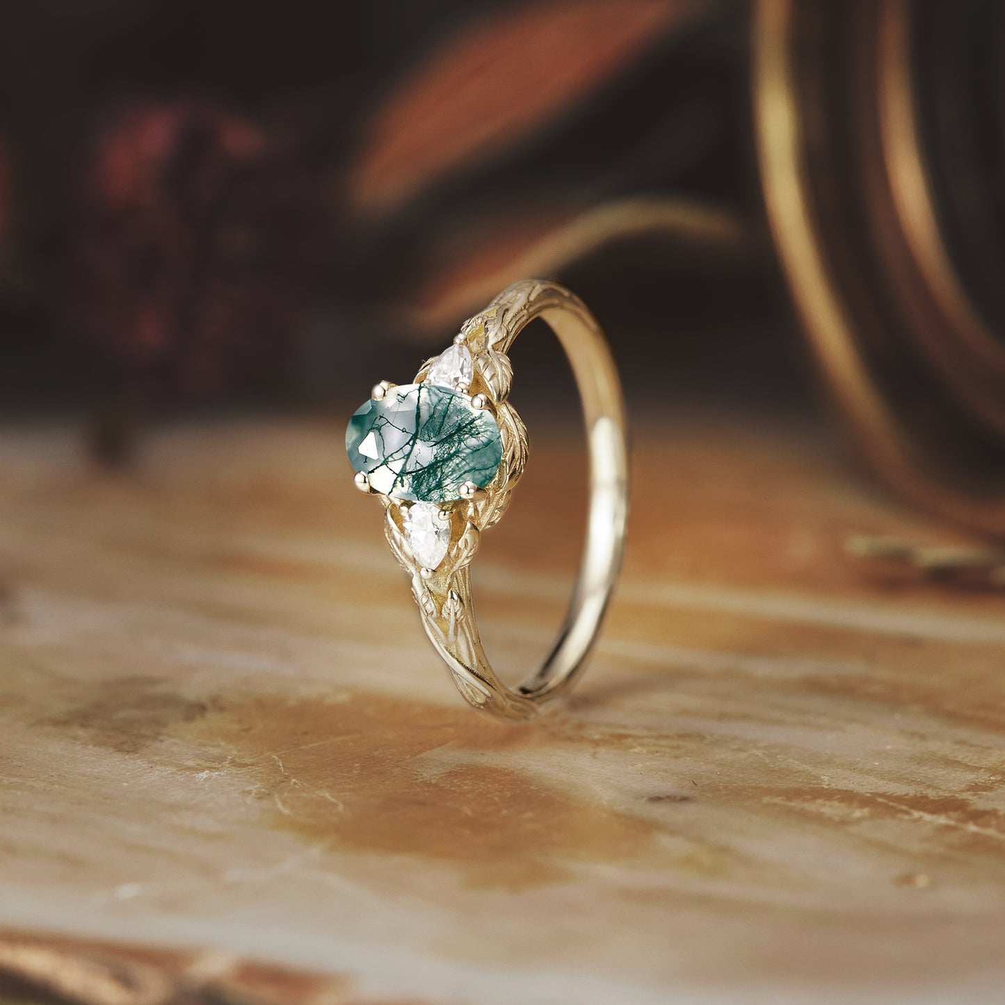 Moss agate engagement ring with detailed band on a rustic wooden background.