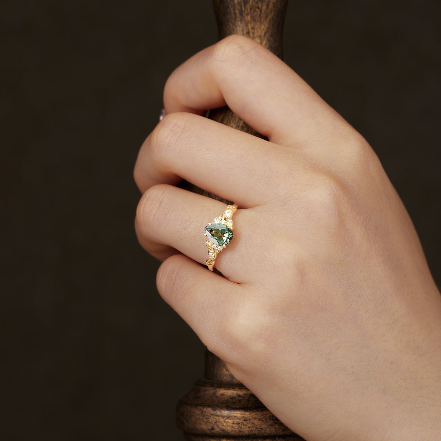 Gold leaf ring showcasing pear-shaped green sapphire elegantly worn on hand.