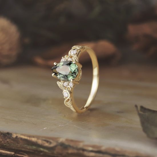 Elegant gold ring featuring pear-shaped green sapphire and intricate leaf motifs