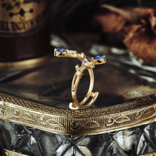 Nature-inspired gold ring with marquise sapphires and moissanite on a decorative tray.