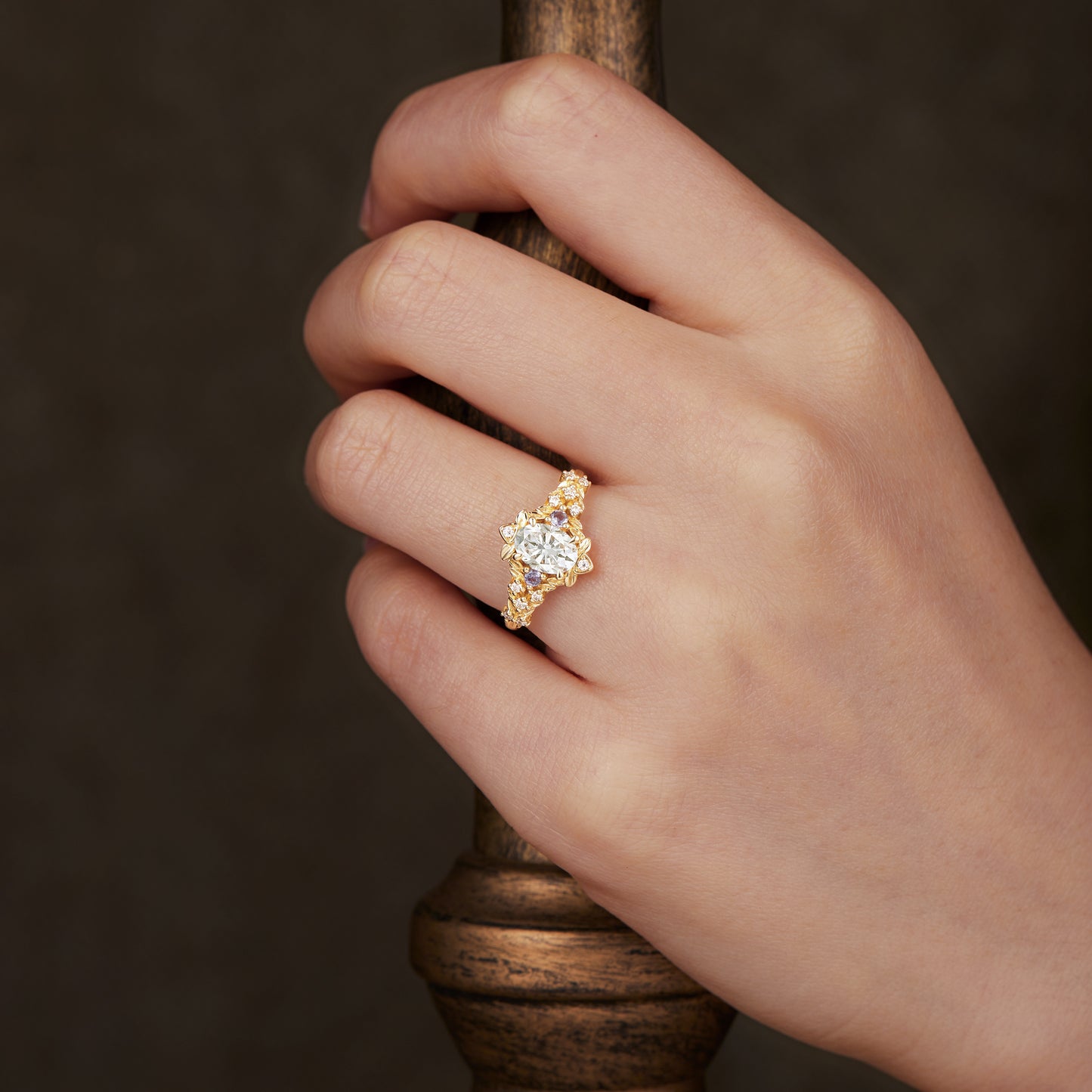 Floral engagement ring with moissanite and tanzanite worn on a hand.