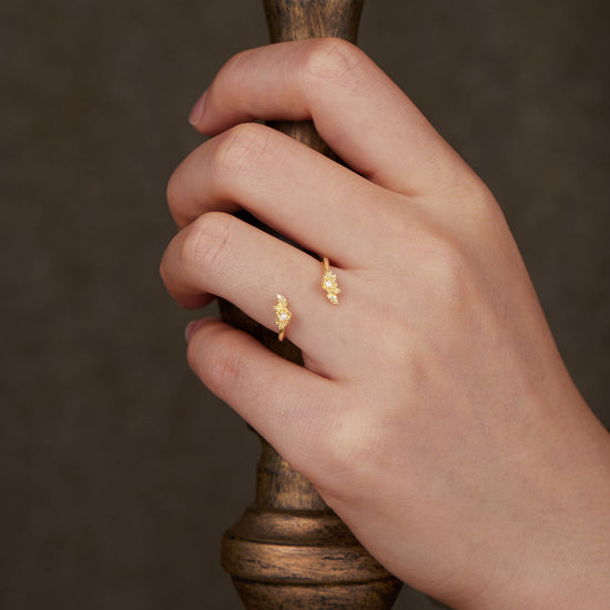 Hand wearing nature-inspired gold wedding rings with floral motifs and sparkling accents.