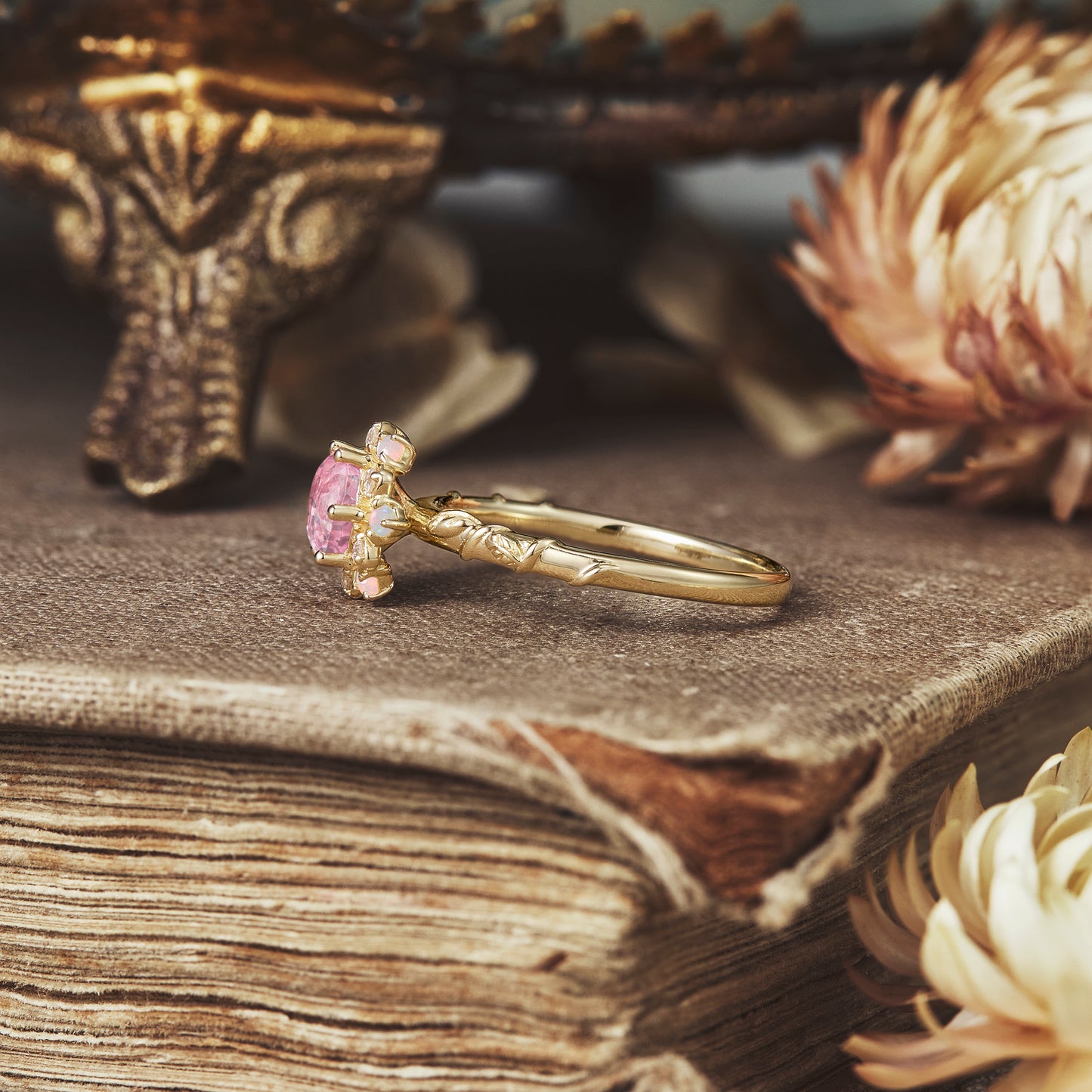 Close-up of halo pink Padparadscha ring on vintage book with moissanite accents.