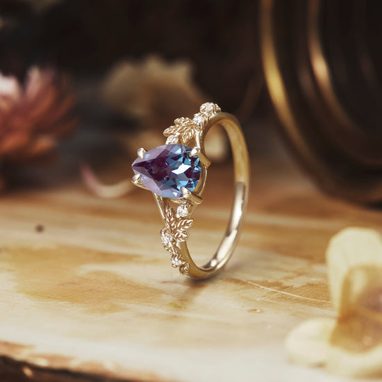 Nature-inspired ring with pear-cut alexandrite and floral details on wooden display.