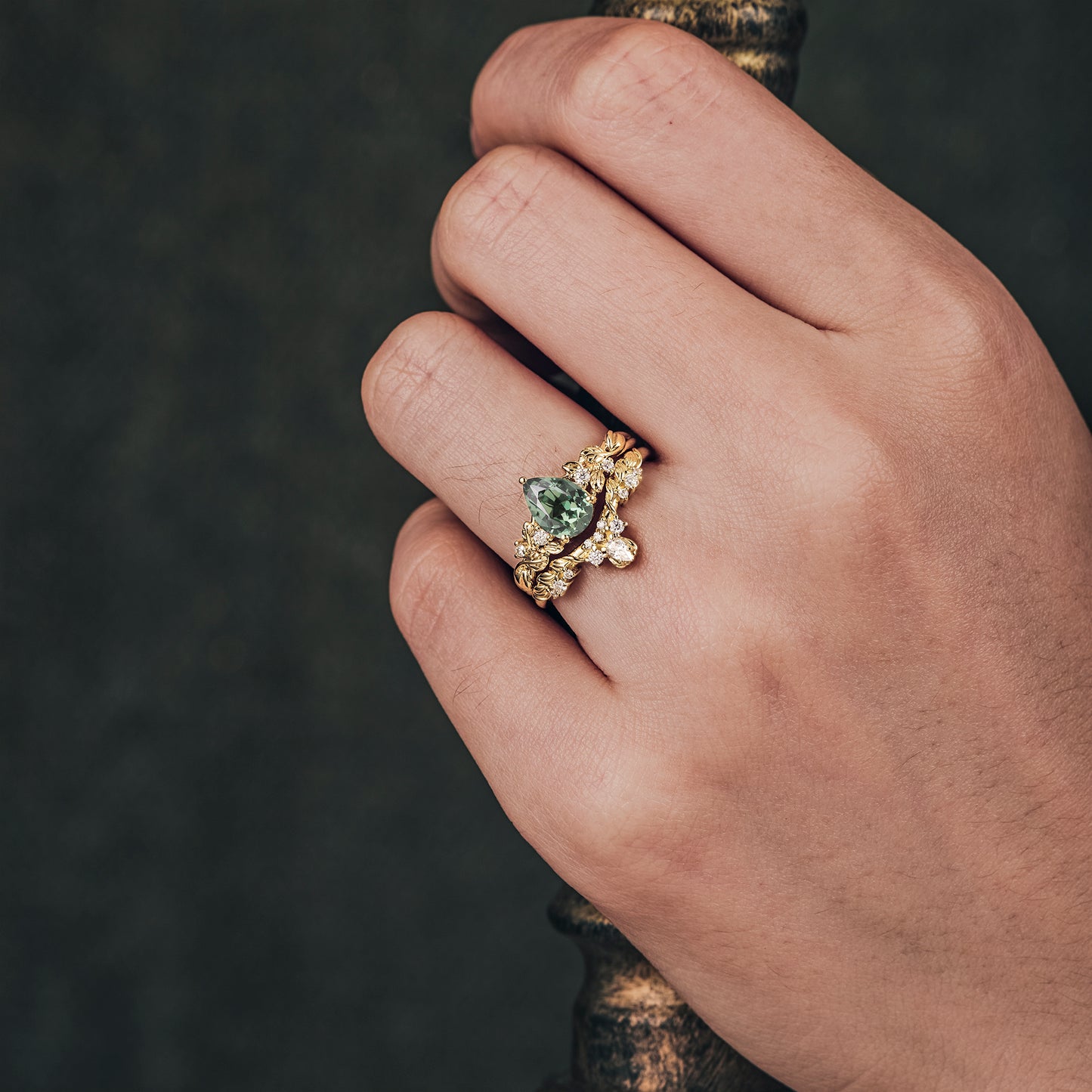 Hand showcasing green sapphire ring set with floral gold design and moissanite accents.