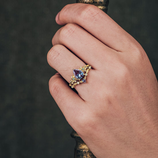 Hand model showcasing pear alexandrite flower ring set with gold floral accents.