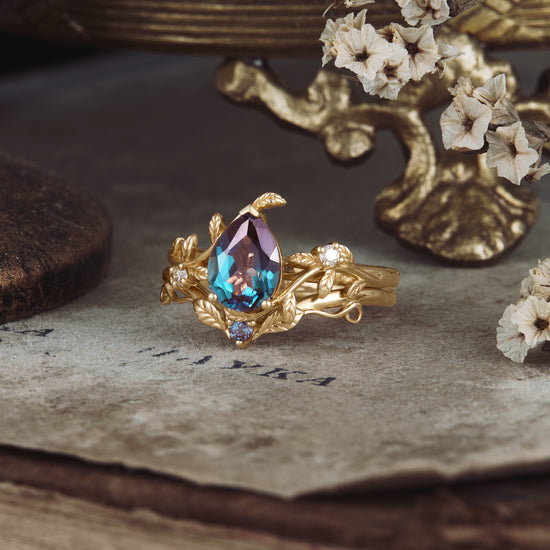 Nature-inspired gold ring set with pear-shaped lab alexandrite and floral moissanite accents.