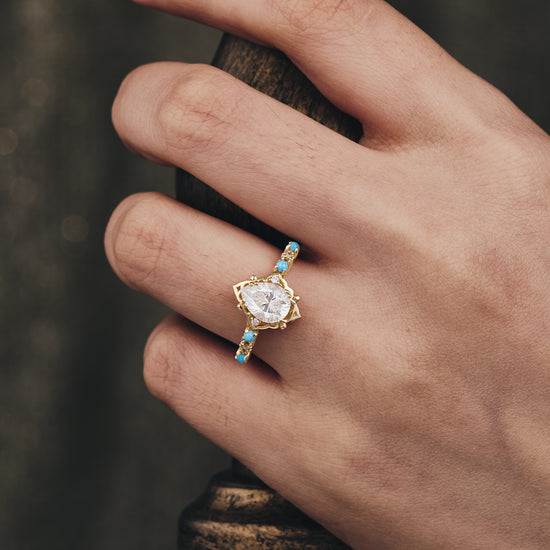 Bohemian turquoise and moissanite pear cut ring on a hand, yellow gold band.