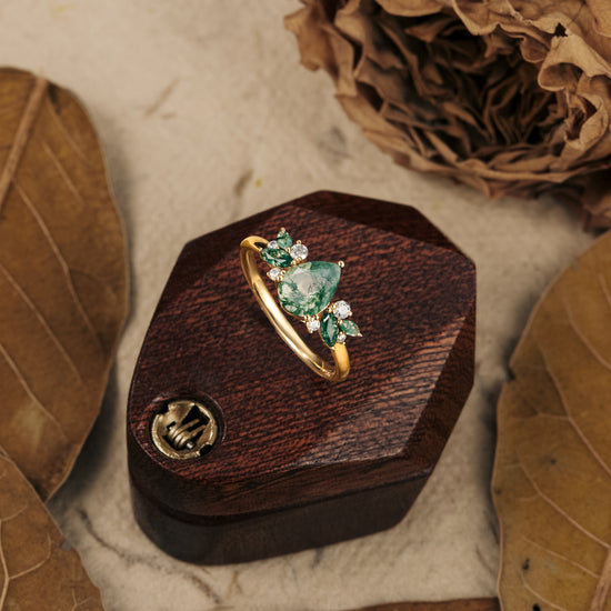 Moss agate pear-cut ring with moissanite accents on wooden display box.